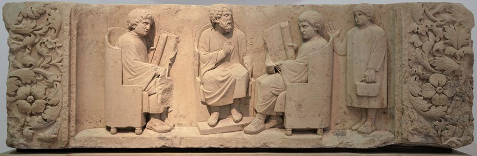 Funerary relief of a Roman school scene, c. 180185 CE. The teacher (centre) instructs two students (seated left and right), who are reading scrolls, while a third younger student enters holding wax tablets bound by a leather strap. Currently held in the Rheinisches Landesmuseum, Trier.